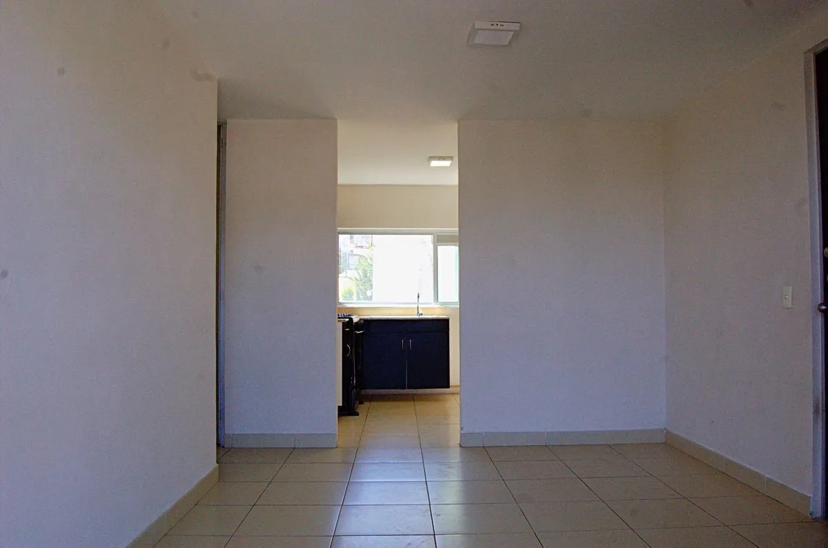Vista desde la estancia a la cocina, con pisos de cerámica, mostrando la cocina semi-equipada al centro, a la izquierda la puerta de acceso al departamento, y a la izquierda el acceso a las recámaras y baño secundario