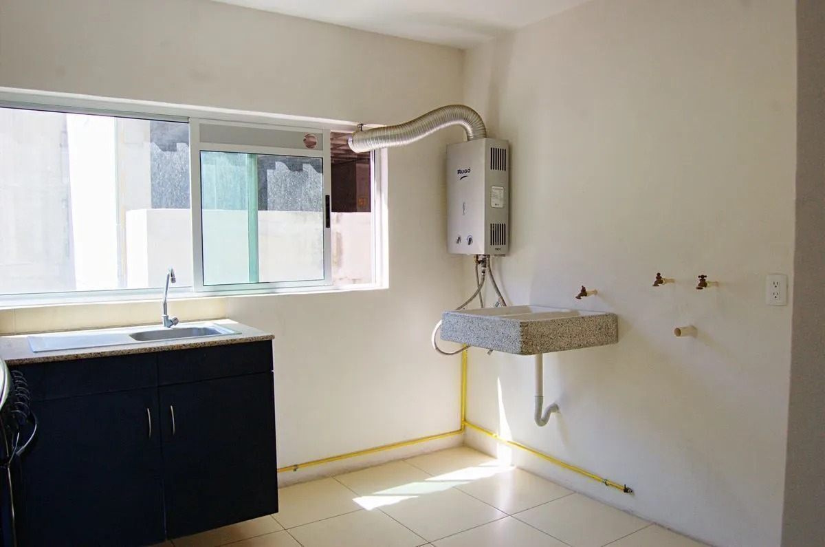 Vista desde la entrada de la cocina con pisos de cerámica, mostrando el área de lavatrastes, ventilación de la cocina, a la derecha se observan las conexiones para centro de lavado, lavadero de granito y calentador de agua con conexion para gases.